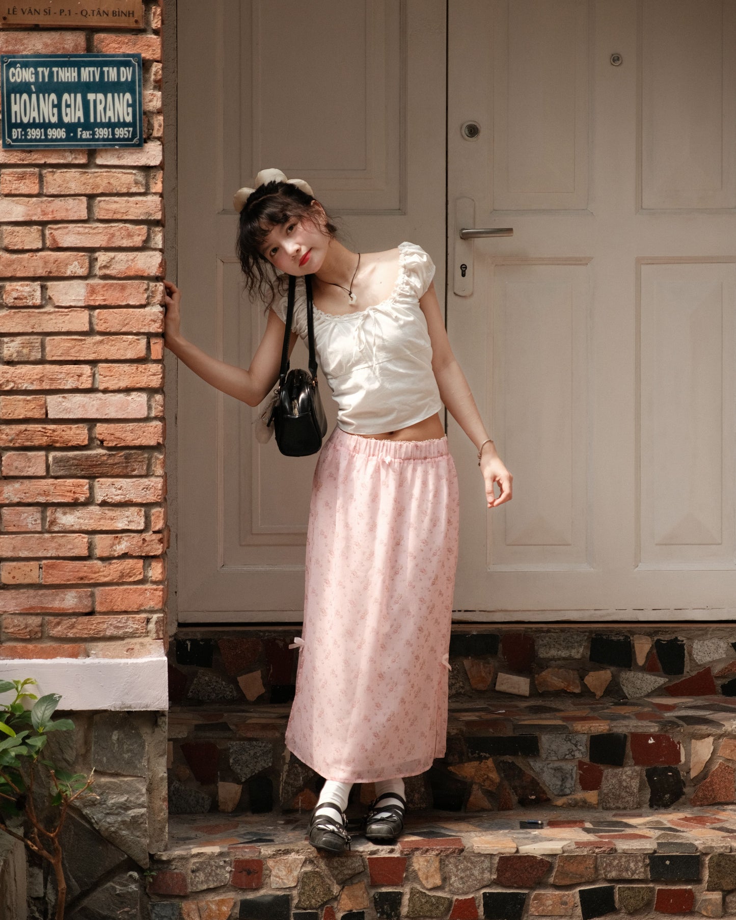 girl wearing cute pink skirt standing on stairs with legs cross and one hand on the wall beside